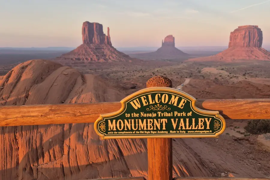 Panneau "Welcome to Monument Valley" avec les célèbres Mittens en arrière-plan, étape mythique d'un voyage moto Route 66